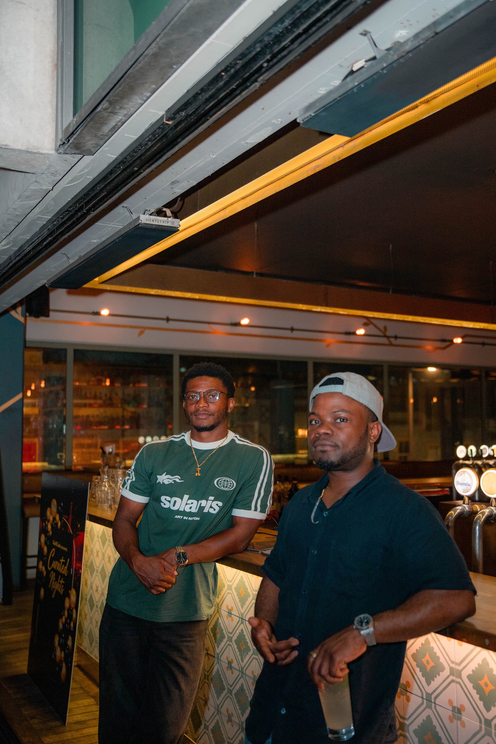 Two guests standing at the bar beside the Curated Nights sign